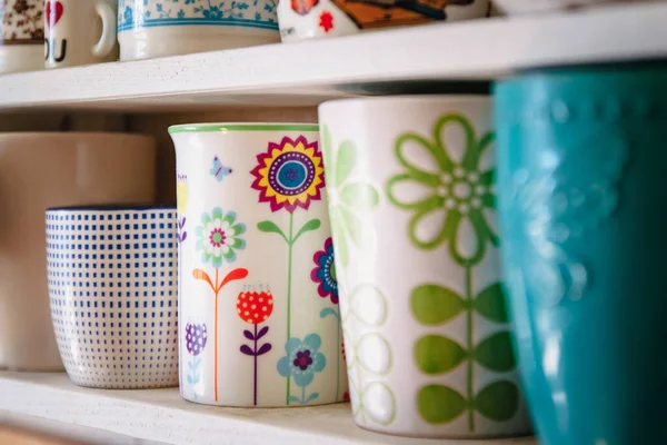 在一个白色的家架子上，一排排站着各种各样的瓷杯和杯子，它们都是春天花色鲜亮的. — 图库照片