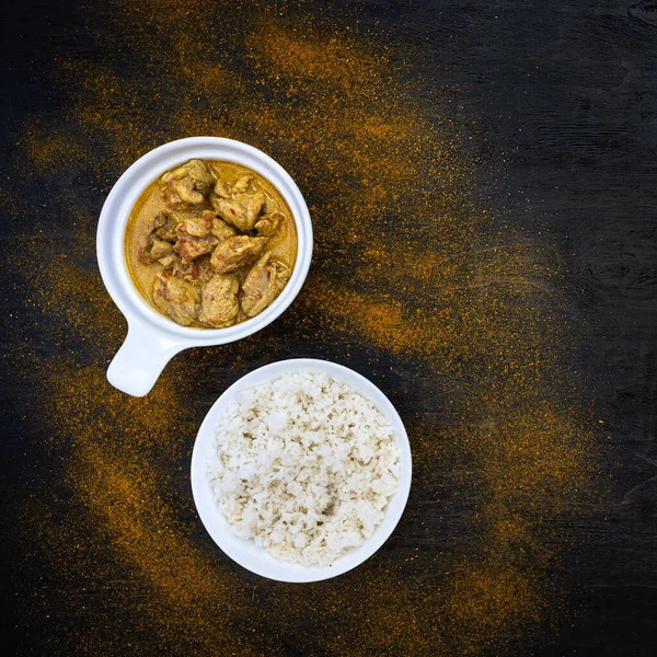 Orange-würziges Hühnercurry und Reis in einfachen weißen Tellern auf dunklem Hintergrund. Um Paprika, Zitrone, Currypulver. Traditionelle indische Küche. Flach lag er. Ansicht von oben, Kopierraum. — Stockfoto