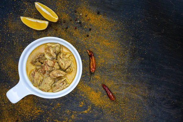 Orange pedas kari ayam di piring putih sederhana pada latar belakang gelap. Sekitar lada panas, lemon, bubuk kari. Masakan tradisional India. Berbaringlah. Tampilan atas, ruang penyalinan . — Stok Foto