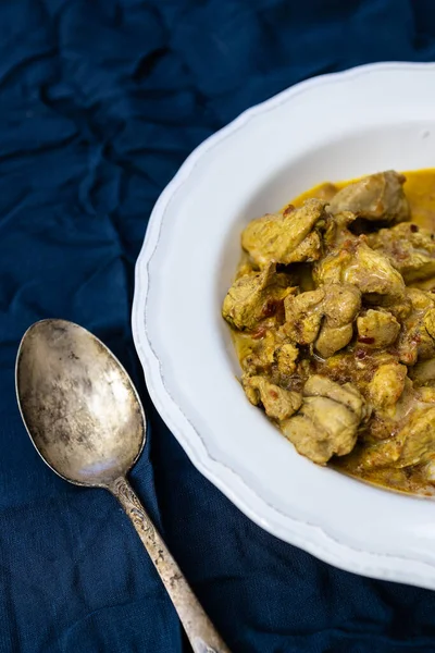 Kari ayam pedas oranye di piring putih dengan latar belakang biru tua. Masakan tradisional India. — Stok Foto