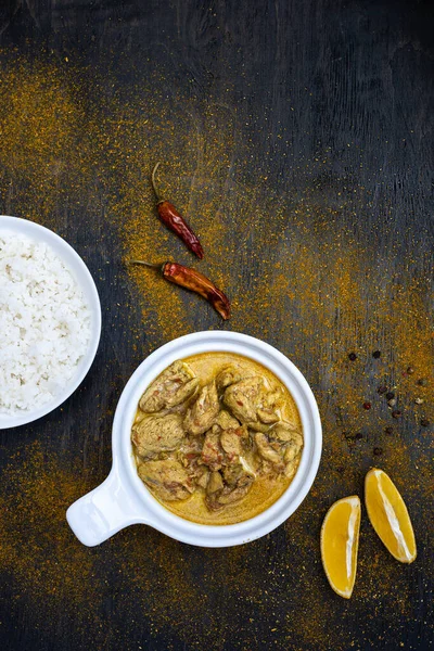 Orange pedas kari ayam dan beras di piring putih sederhana pada latar belakang gelap. Sekitar lada panas, lemon, bubuk kari. Masakan tradisional India. Berbaringlah. Tampilan atas, ruang penyalinan . — Stok Foto