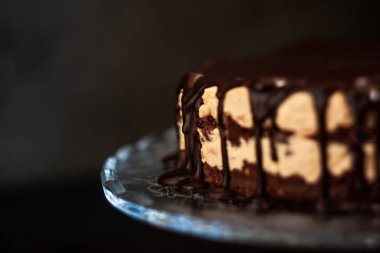 Koyu ahşap zemin üzerinde çikolata damlayan tereyağlı fındık kremalı çikolata katmanları. Minimalizm, uzayı kopyala. Seçici odak, yakın plan.