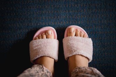 Pembe tüylü terlikleri ve koyu mavi halı arka planında pedikür yaptıran kadın bacakları. Boşluğu, düzlüğü, minimalizmi kopyala.