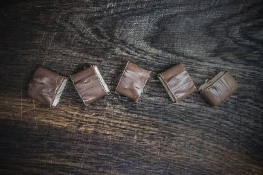 Paramparça kesilmiş bir çikolata, koyu ahşap bir arka planda yatıyor. Uzayı kopyala, düz yat.