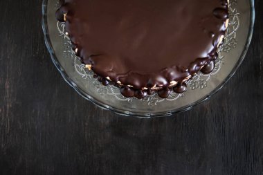 Koyu ahşap arka planda cam bir standın üzerinde çikolatalı pasta. Düzlük, minimalizm, simetri. Boşluğu kopyala