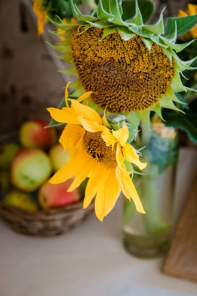 A bouquet with rustic flowers a sunflower stands on a table near a basket with red apples