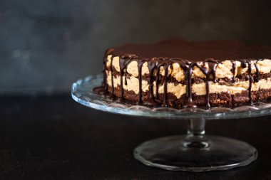 Koyu ahşap zemin üzerinde çikolata damlayan tereyağlı fındık kremalı çikolata katmanları. Minimalizm, uzayı kopyala. Seçici odak, yakın plan.