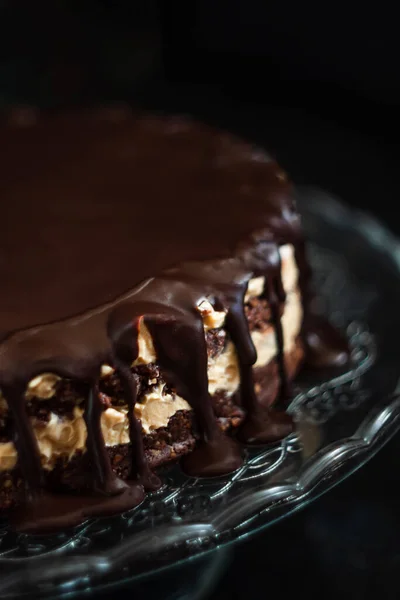 Шоколадные круглые слои торта со сливками сливочно-кремового ореха с шоколадными капельницами на стеклянном подставке на темном деревянном фоне. Минимализм, скопируй пространство. Селективный фокус, крупный план . — стоковое фото