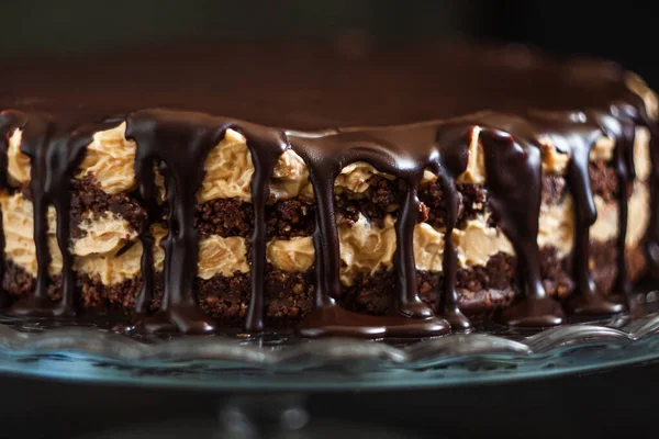 Шоколадные круглые слои торта со сливками сливочно-кремового ореха с шоколадными капельницами на стеклянном подставке на темном деревянном фоне. Минимализм, скопируй пространство. Селективный фокус, крупный план . — стоковое фото