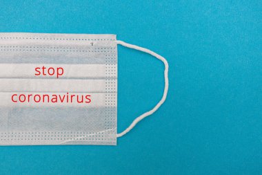 Mavi arka planda, Coronavirus covid 19 yazan tek kullanımlık tıbbi maske. Dünya pandemik koronavirüsü. Salgını durdurun. Sağlık ve gribin önlenmesi ve bulaşıcı