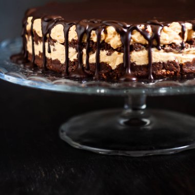 Koyu ahşap zemin üzerinde çikolata damlayan tereyağlı fındık kremalı çikolata katmanları. Minimalizm, uzayı kopyala. Seçici odak, yakın plan.