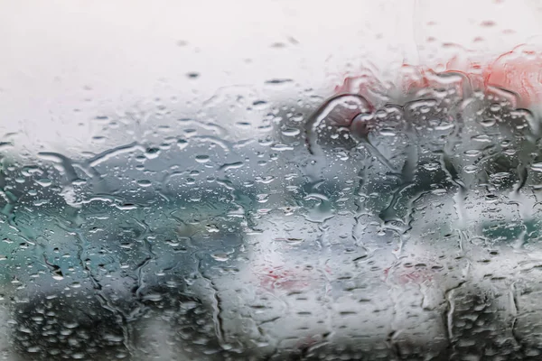 O trânsito fica parado, em um dia frio e úmido, disparado através de um pára-brisas, com foco nas gotas de chuva, luzes fora de foco. Vista da janela de vidro do carro. Conceptual mau tempo fundo . — Fotografia de Stock