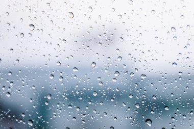 Yağmur mevsiminde ıslak pencere camının üzerine yağmur damlaları düşer. Soyut arkaplan. Bulutlu bir ortamda, bulanık şehirden izole edilmiş doğal yağmur damlaları..