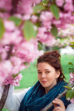 Ukrayna 'nın Kiev kentindeki şehir parkında çiçek açan pembe sakura ağacının altında beyaz süveter ve mavi eşarplı mutlu, kızıl saçlı genç bir kadının portresi görülüyor..