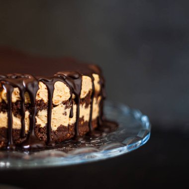 Koyu ahşap zemin üzerinde çikolata damlayan tereyağlı fındık kremalı çikolata katmanları. Minimalizm, uzayı kopyala. Seçici odak, yakın plan.