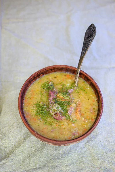 Pea soup with smoked meat, crackers and herbs in a rustic clay plate on a light linen tablecloth. Minimalism Life style, naturalness. Copy space. — Stock Photo, Image