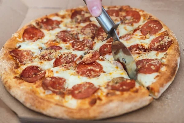 Coupé à la main masculine pizza margarita avec pepperoni avec un couteau spécial, gros plan — Photo