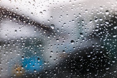 Yağmur mevsiminde ıslak pencere camının üzerine yağmur damlaları düşer. Soyut arkaplan. Bulutlu bir ortamda, bulanık şehirden izole edilmiş doğal yağmur damlaları..