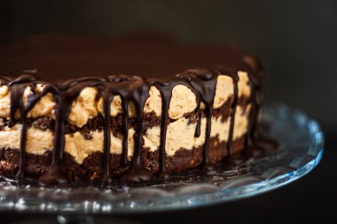 Koyu ahşap zemin üzerinde çikolata damlayan tereyağlı fındık kremalı çikolata katmanları. Minimalizm, uzayı kopyala. Seçici odak, yakın plan.