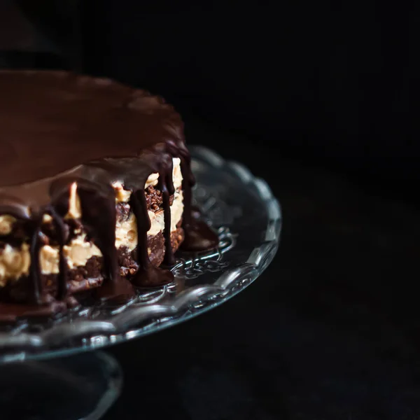 Schokoladenrunde Kuchenschichten mit Butter-Sahne-Nuss-Creme mit Schokoladentropfen auf einem Glasständer auf dunklem Holzgrund. Minimalismus, Kopierraum. Selektive Fokussierung, Nahaufnahme. — Stockfoto