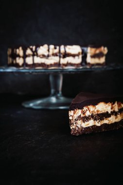 Koyu ahşap zemin üzerinde çikolata damlayan tereyağlı fındık kremalı dilimler ve çikolatalı pasta katmanları. Minimalizm, uzayı kopyala. Seçici odak, yakın plan.