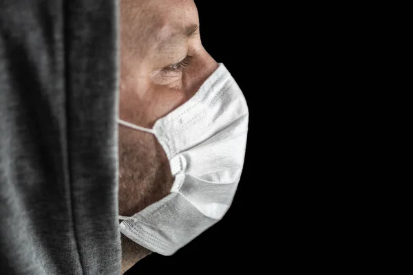 Young tired man in a hood and a medical mask looks forward against a dark background. Copy space. Close-up portrait in profile. Concept, World pandemic coronavirus. Stop the coronavirus epidemic. Health and prevention of influenza and an infectious o
