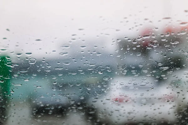 Traffic stands still, on a cold, wet day, shot through a windscreen, focusing on the rain droplets, tailights out of focus. View from car glass window. Conceptual bad weather background.