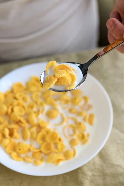 Un uomo ritagliato tiene un cucchiaio in cornflakes con latte in un piatto bianco su una tovaglia ruvida pianura. Vista dall'alto. Concetto, semplice veloce colazione americana sana — Foto Stock