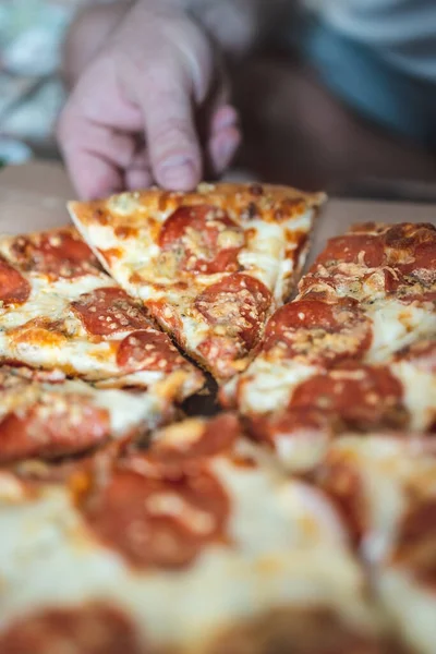 Um lavrador leva um pedaço de pizza com a mão. Foco seletivo, borrão, close-up . — Fotografia de Stock