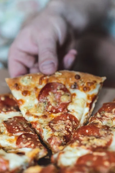 Cropped man prend un morceau de pizza avec sa main. Concentration sélective, flou, gros plan . — Photo