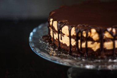 Koyu ahşap zemin üzerinde çikolata damlayan tereyağlı fındık kremalı çikolata katmanları. Minimalizm, uzayı kopyala. Seçici odak, yakın plan.