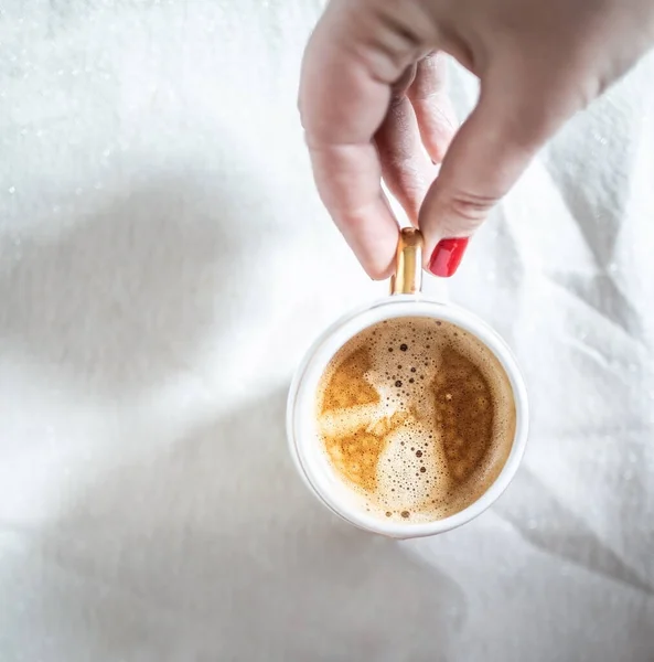 Manos femeninas recortadas con manicura roja sostienen un mandril con café capuchino sobre un fondo descuidado retro blanco claro. Copiar espacio. Piso tendido, vista superior . — Foto de Stock