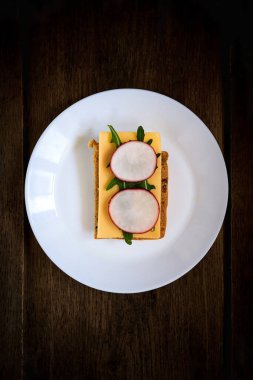 Çavdar ekmeğinden, sert peynirden, turptan, roka 'dan yapılmış sandviç, beyaz bir tabakta koyu ahşap arka planda servis ediliyor. Simetri. Uzayı kopyala Düz yerde, üst tarafta. Yakın plan.