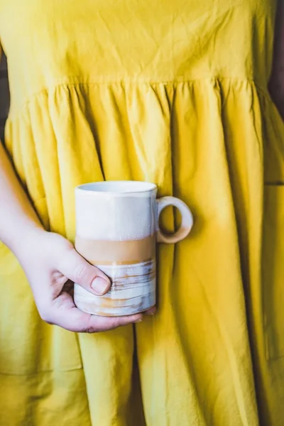 Cropped jeune femme blanche dans une robe de lin jaune simple tient dans ses mains une tasse en céramique d'argile d'une forme originale faite à la main. Espace de copie. Évolution — Photo