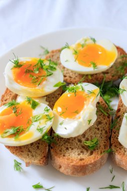 Beyaz bir tabakta tam tahıllı tost ekmeğine dereotlu rafadan yumurta yarıları. Yakın çekim, üst görüş. Sağlıklı, sağlıklı ve sağlıklı kahvaltı konsepti.