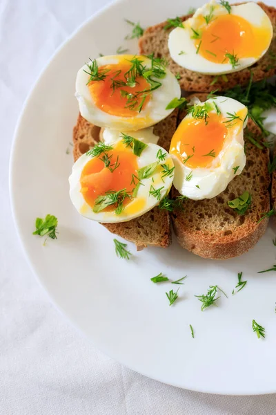Soft-boiled egg halves with dill on whole grain toast bread on a white plate. Close-up, top view. Healthy, healthy and healthy breakfast concept. — Stock Photo, Image