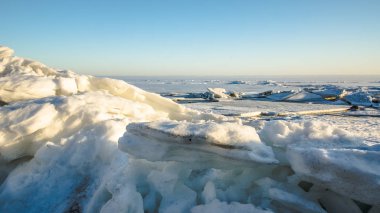 Icy snow-covered hummocks. Bright sun on a light pink cloudy sky over the Natural winter background. 