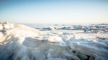 Icy snow-covered hummocks. Bright sun on a light pink cloudy sky over the Natural winter background. 