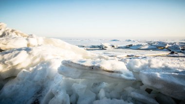 Icy snow-covered hummocks. Bright sun on a light pink cloudy sky over the Natural winter background. 