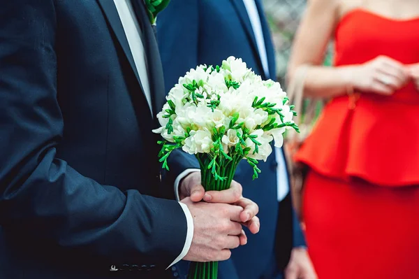 Verloofde in een donker blauwe pak houdt een bruiloft boeket gemaakt van witte bloemen — Stockfoto