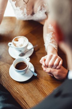 Gelin ve damat yuvarlak ahşap masa, bir kafede kahve içme. hafifçe birbirlerinin tutan eller
