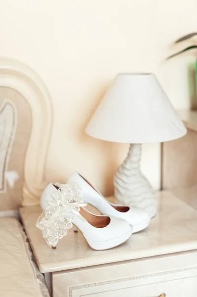 テーブル ランプの横にある台座の上のかかとの白い結婚式の靴。明るい色ですべて — ストック写真