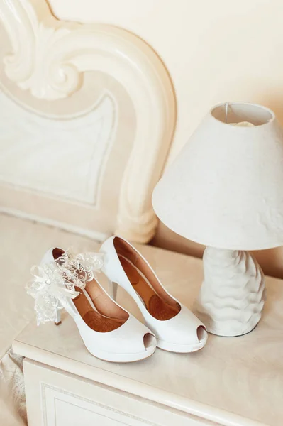 Scarpe da sposa bianche con tacchi su un piedistallo accanto a una lampada da tavolo. Il tutto in colori vivaci — Foto Stock