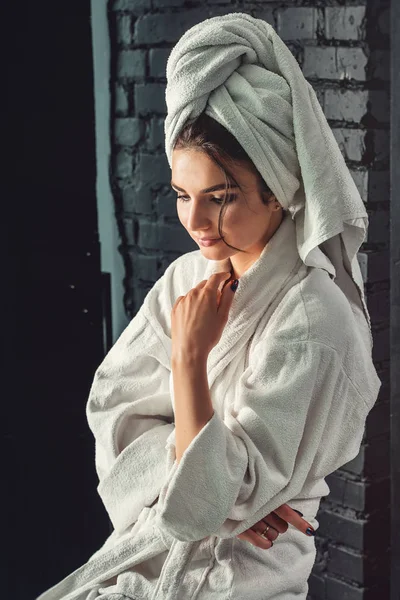 Sexy chica joven con el pelo oscuro, ojos grandes y cejas oscuras con bata de baño blanco con toalla en la cabeza . — Foto de Stock