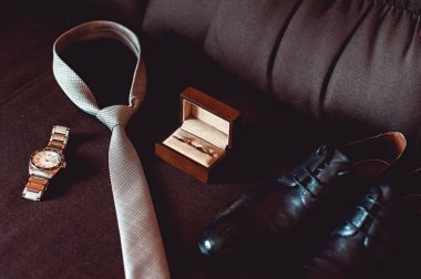 Modern damat aksesuarları, yakın çekim. Alyans kahverengi ahşap kutu, kravat, deri ayakkabı ve izle