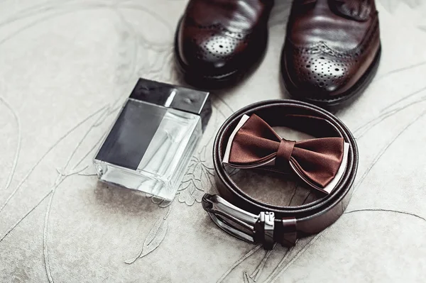 Brown bow tie, perfume, leather shoes and belt. Grooms wedding morning. Close up of modern man accessories
