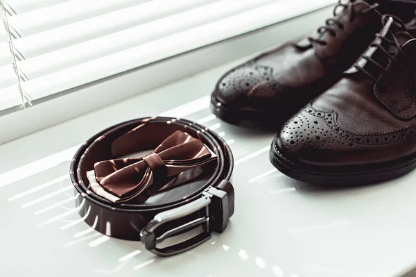 Brown bow tie, leather shoes and belt. Grooms wedding morning. Close up of modern man accessories