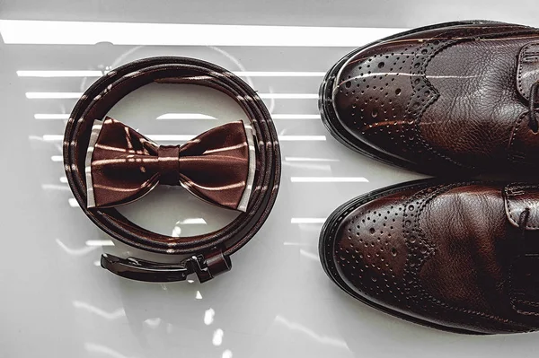 Brown bow tie, leather shoes and belt. Grooms wedding morning. Close up of modern man accessories