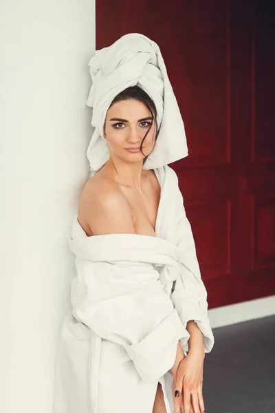 Сексуальна молода дівчина з темним волоссям, великими очима і темними бровами в білому халаті для ванни з рушником на голові . — стокове фото