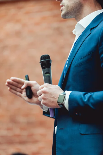 Üzleti és beszéd téma: ember-kék öltöny kezében egy szürke mikrofon egy narancs tégla háttér — Stock Fotó